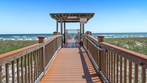 A wooden boardwalk leading to a beach with a wooden pergola and a sign. - Beach Colony Tower 14A | Oceanfront | Resort Amenities | Beach Getaways (Pensacola)