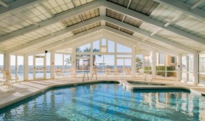 Une piscine intérieure à l’eau d’un bleu cristallin, entourée de chaises longues et dotée d’un toit en verre.