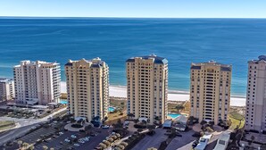A high-rise hotel with multiple floors, a parking area, and a view of the ocean. - Beach Colony Tower 14A | Oceanfront | Resort Amenities | Beach Getaways (Pensacola)