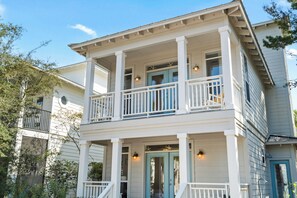 A two-story house with a balcony, a front porch, and a blue door. - SeaQuinn Beach House in 30A | 12,000 sq' Resort Pool | 4 Bikes | My Beach Getaways (Seacrest Beach)