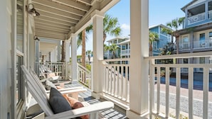 A covered porch with white railings, outdoor seating, and a view of a blue building with balconies.