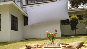 An outdoor dining area with a wooden table set for two, surrounded by colorful cushions and a blanket. - The Dream House  (Quito)