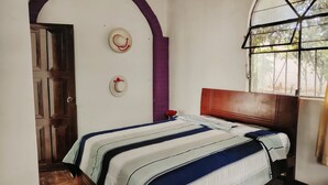 A bedroom with a bed, a wooden door, a window with a view, and a wall with two decorative hats. - The Dream House  (Quito)