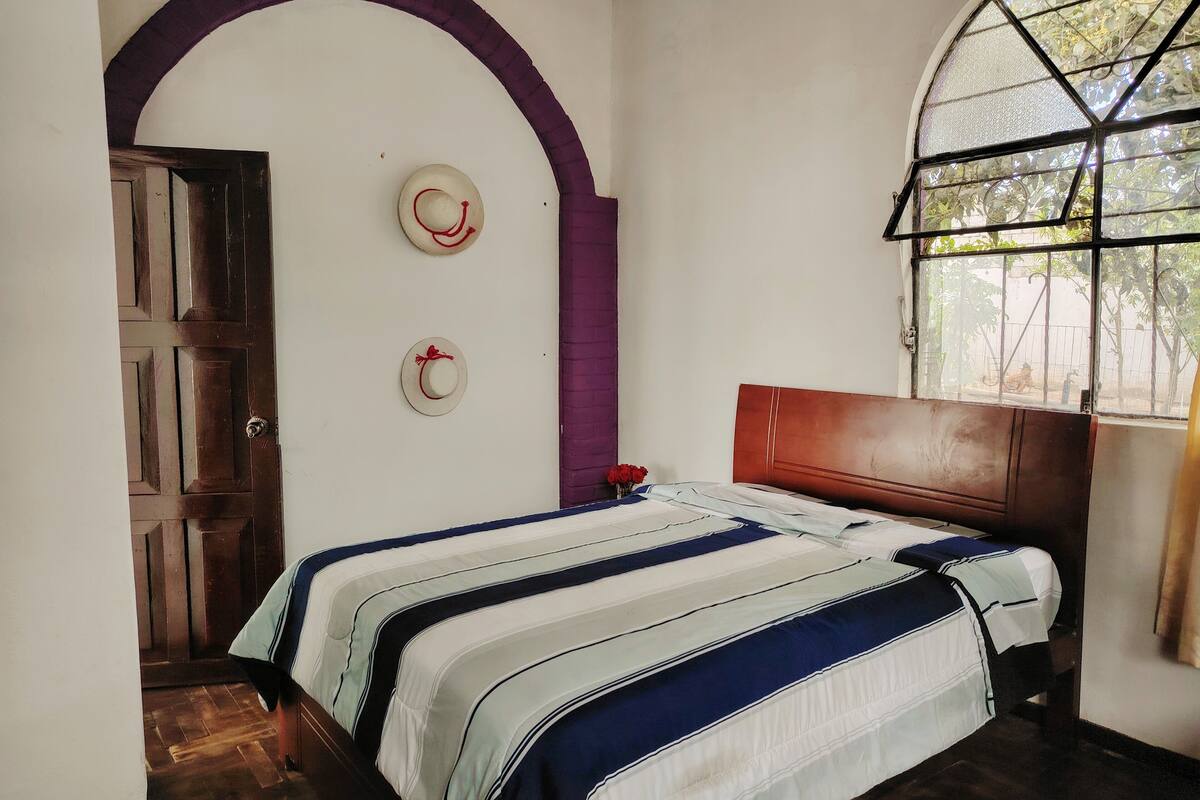 A bedroom with a bed, a wooden door, a window with a view, and a wall with two decorative hats.