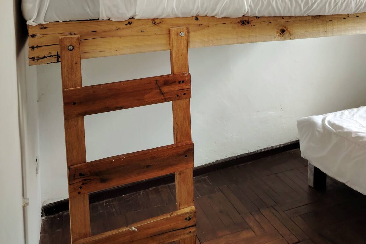 A bunk bed with a wooden ladder, white bedding, and a wooden ceiling.