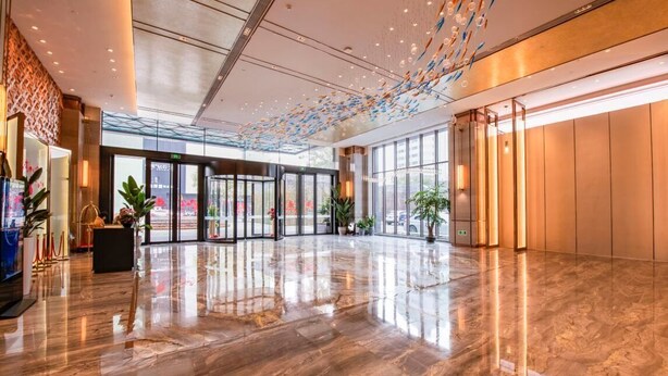 A spacious lobby with a polished marble floor, large glass doors, and a ceiling with hanging decorative elements.