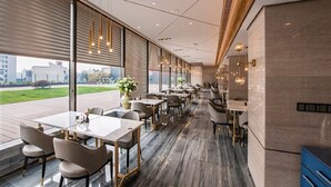 A modern restaurant with a long dining area, large windows, and a view of the outdoors.