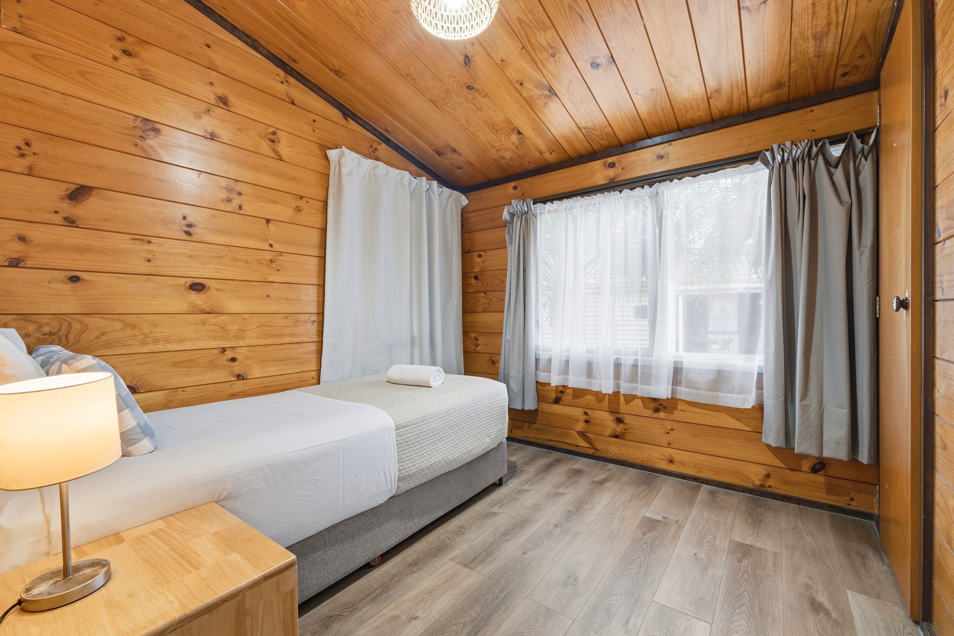 A wooden cabin room with two beds, a nightstand, and a window with curtains.