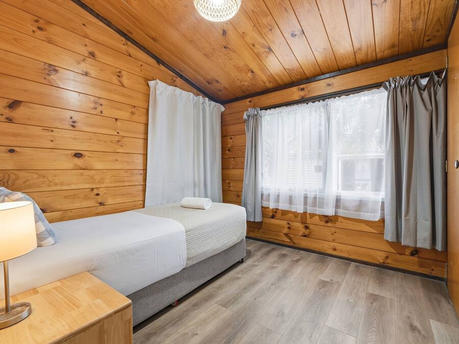 Quarto de cabana de madeira com duas camas, uma mesa de cabeceira e uma janela com cortinas.