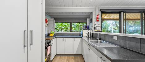 Une cuisine moderne avec des meubles blancs, un plan de travail noir et une vue sur la verdure à l’extérieur.