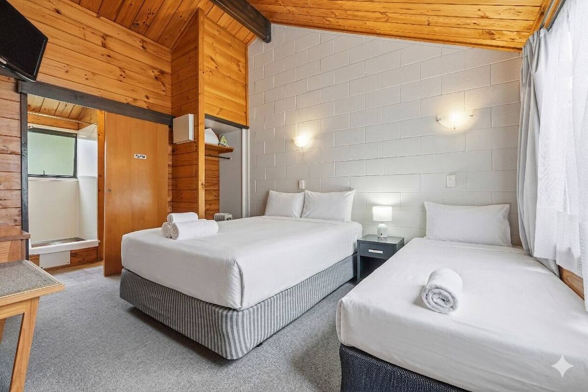 A hotel room with two beds, a wooden ceiling, white brick walls, and a small table.