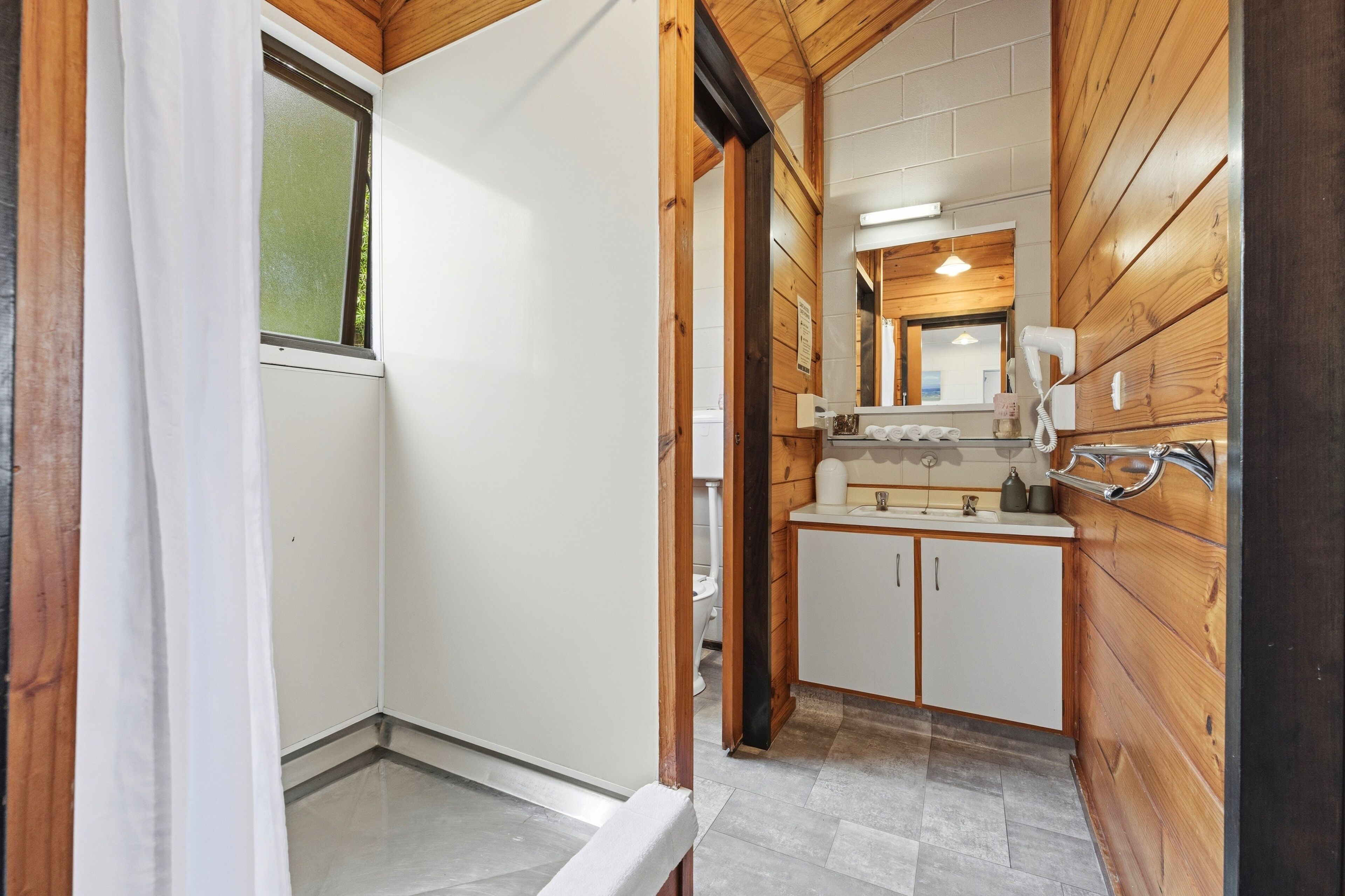 A narrow hallway with wooden walls, a white door, and a window with a curtain.