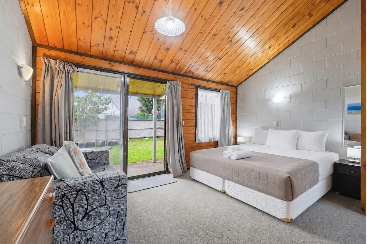 A room with a bed, a sofa, a table, and a sliding glass door leading to a patio.
