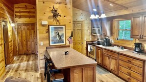 A wooden cabin interior with a kitchen area featuring a wooden island, bar stools, a framed fish picture, and a flag. - Timber Ridge Lodge -HOT TUB- POOL (Harpers Ferry)