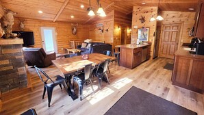 A rustic cabin interior with a wooden dining table, chairs, a sofa, a kitchen area, and a fireplace. - Timber Ridge Lodge -HOT TUB- POOL (Harpers Ferry)