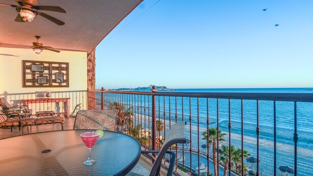 Un balcon avec vue sur la mer, une table avec une boisson et des sièges.