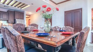 Une salle à manger avec une table en bois dressée pour six personnes, entourée de chaises à motifs. Un vase rempli de fleurs rouges est posé sur la table.