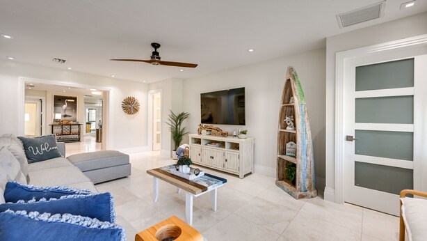 A modern living room with a grey sofa, blue cushions, a wooden coffee table, and a television on a cabinet. - Updated Naples Retreat w/ Private Pool & Patio! (Naples)
