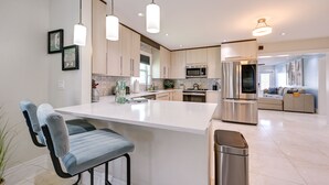 A modern kitchen with a central island, stainless steel appliances, pendant lighting, and a view into the living area. - Updated Naples Retreat w/ Private Pool & Patio! (Naples)
