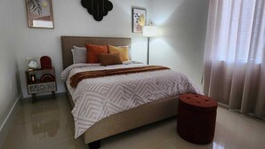 A modern bedroom with a large bed, a bedside table with a lamp, and a red ottoman. - We are located in the heart of Miami, 10 min away from Downtown, Beaches, M.I.A (Miami)