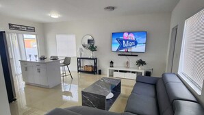 A modern living room with a large sectional sofa, a flat-screen TV, and a kitchen area in the background. - We are located in the heart of Miami, 10 min away from Downtown, Beaches, M.I.A (Miami)