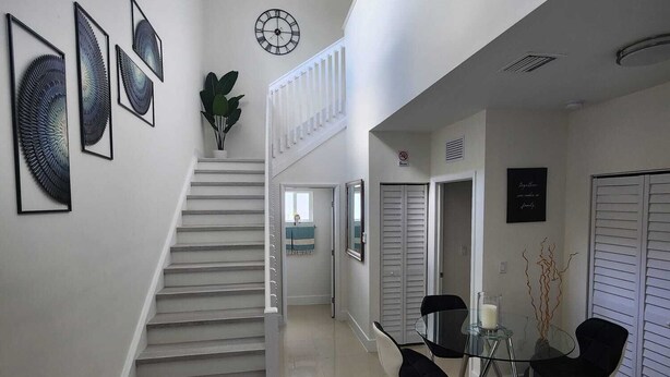 A modern interior with a staircase, a dining area with a glass table and chairs, and a wall with framed artwork. - We are located in the heart of Miami, 10 min away from Downtown, Beaches, M.I.A (Miami)
