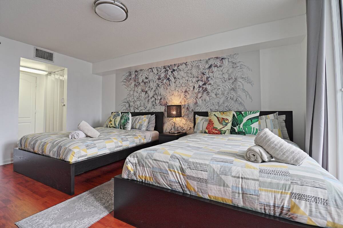 Quarto de hotel com duas camas, uma grande obra de arte abstrata na parede e uma porta visível.