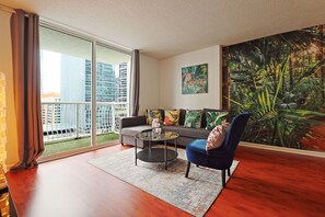 A modern living room with a large window, a sofa, a coffee table, and a painting of a jungle scene. - OneLuxStay in the Heart of Brickell (Miami)
