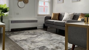 A modern living room with a grey sofa, a patterned rug, and wall art.