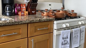 A kitchen with wooden cabinets, a gas stove, copper cookware, a coffee maker, and a knife block.