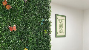 A dining area with a green wall adorned with colorful butterfly decorations, a framed 'Lucky You' sign, and a neatly set dining table with white plates and cutlery.