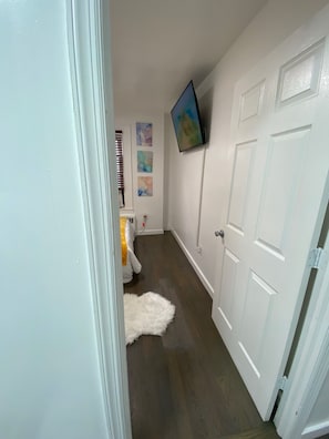 Un couloir avec une porte blanche, un téléviseur fixé au mur et un piano au fond.