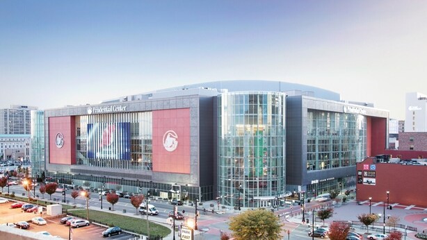 A modern building with a prominent logo on the facade, large glass windows, and a parking lot in front.