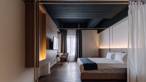 A modern hotel room with a wooden floor, a bed with white linens, a desk with a chair, and a TV mounted on the wall. - Impiana by Roxy Hotel  (Kuching)