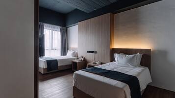 A hotel room with two beds, a wooden ceiling, a large window with curtains, and a bedside table with a lamp.