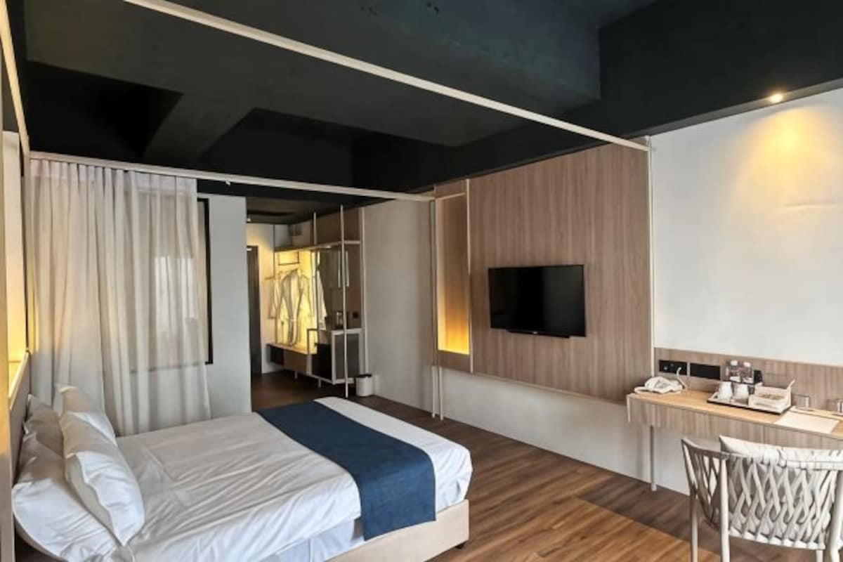 A modern hotel room with a bed, a desk, a TV, and a wardrobe.