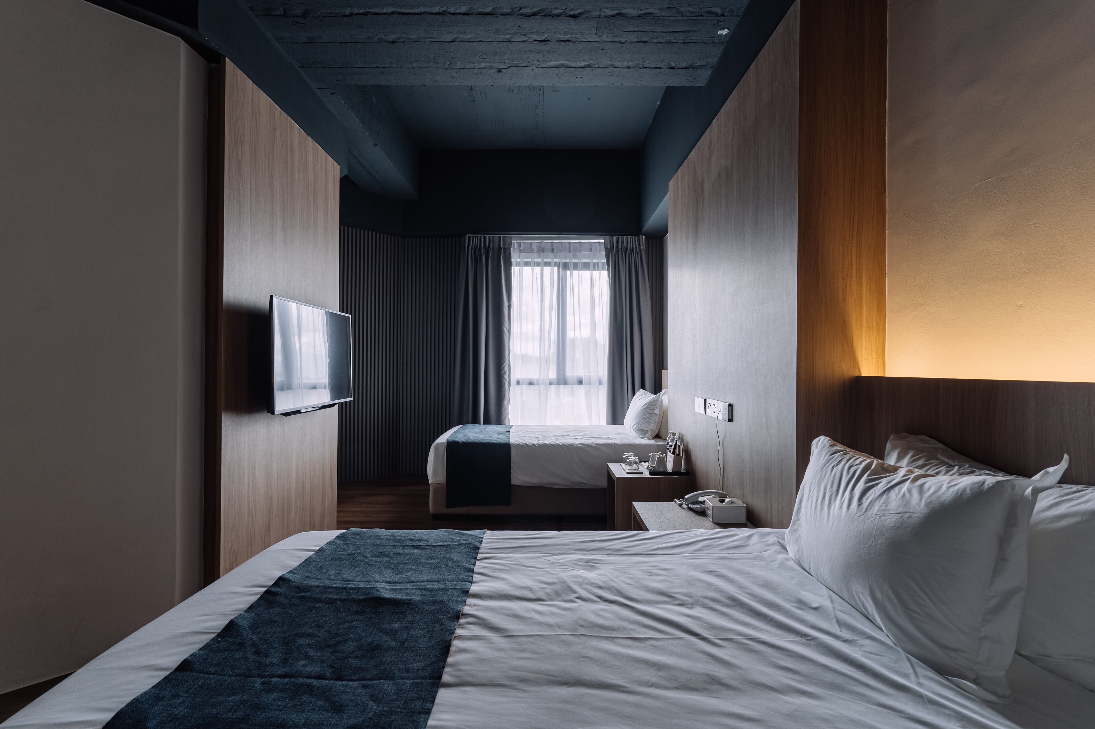 A hotel room with a bed, a TV, a bedside table, and a window with curtains.