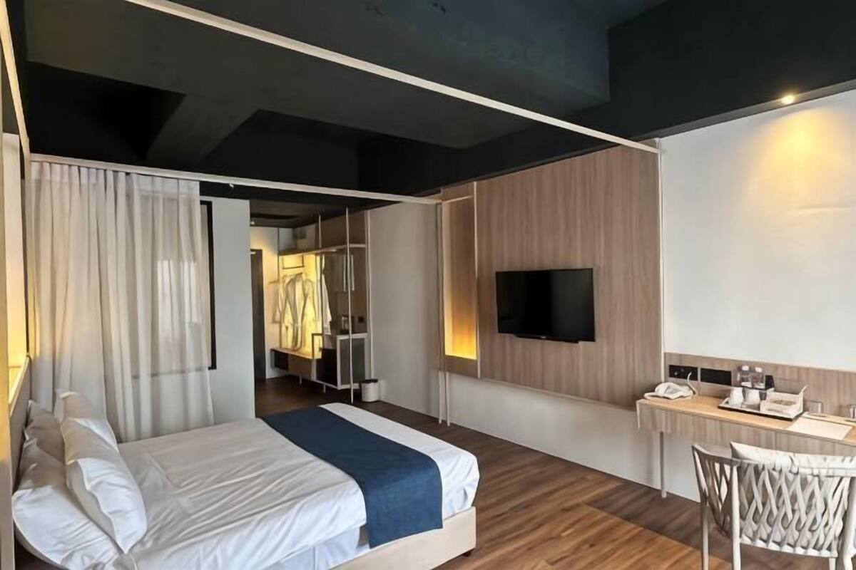 A modern hotel room with a bed, a desk, a TV, and a wardrobe.
