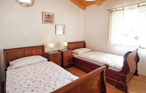 Ein Schlafzimmer mit zwei hölzernen Betten, einem Nachttisch mit Lampe und einem Fenster mit Vorhängen.