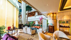 Um lobby espaçoso com teto alto, área de estar central com sofás e poltronas, balcão de recepção e vista dos andares superiores.