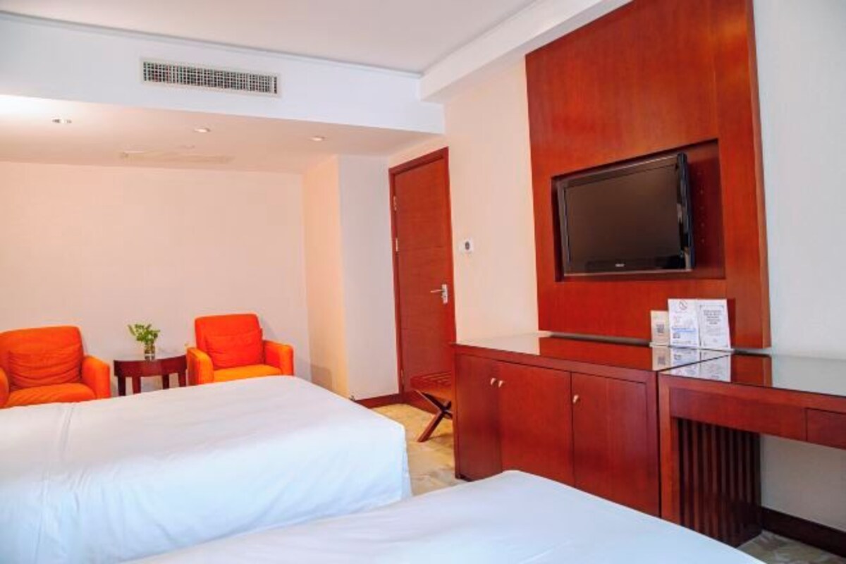 Ein Hotelzimmer mit zwei Betten, einem an der Wand montierten Fernseher und einem Holztisch mit Stuhl.