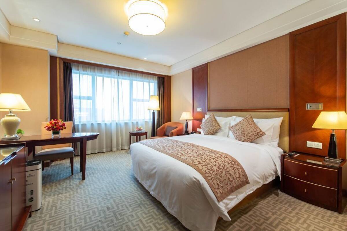 Habitación de hotel con una cama grande, dos mesitas de noche, un escritorio con silla, una ventana con cortinas y suelo alfombrado.