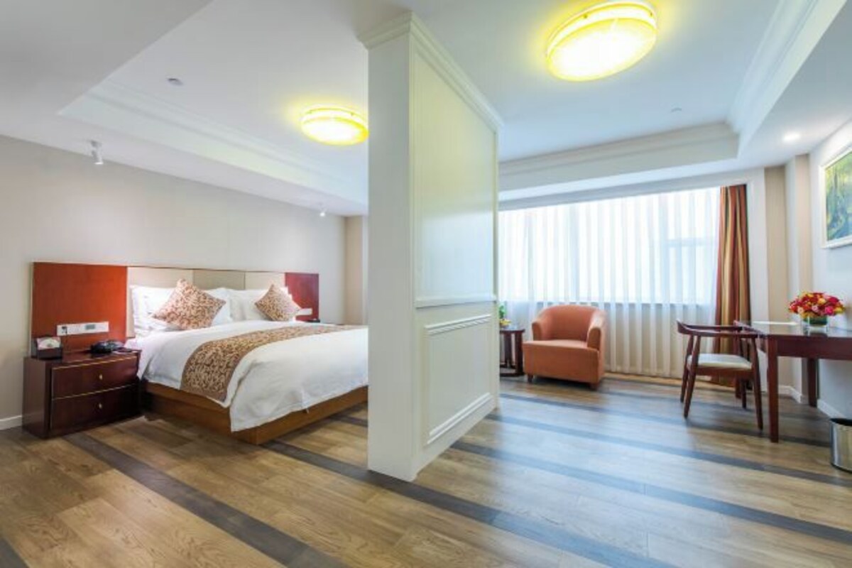 Ein Hotelzimmer mit einem großen Bett, einem Schreibtisch, einem Stuhl und einem Fenster mit Jalousien.