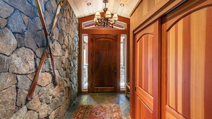 A wooden hallway with a stone wall, a wooden door, and a chandelier.