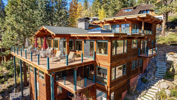 A multi-story wooden cabin with a deck, large windows, and a stone pathway.