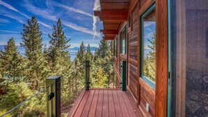 A wooden cabin with a deck overlooking a forest and a lake.