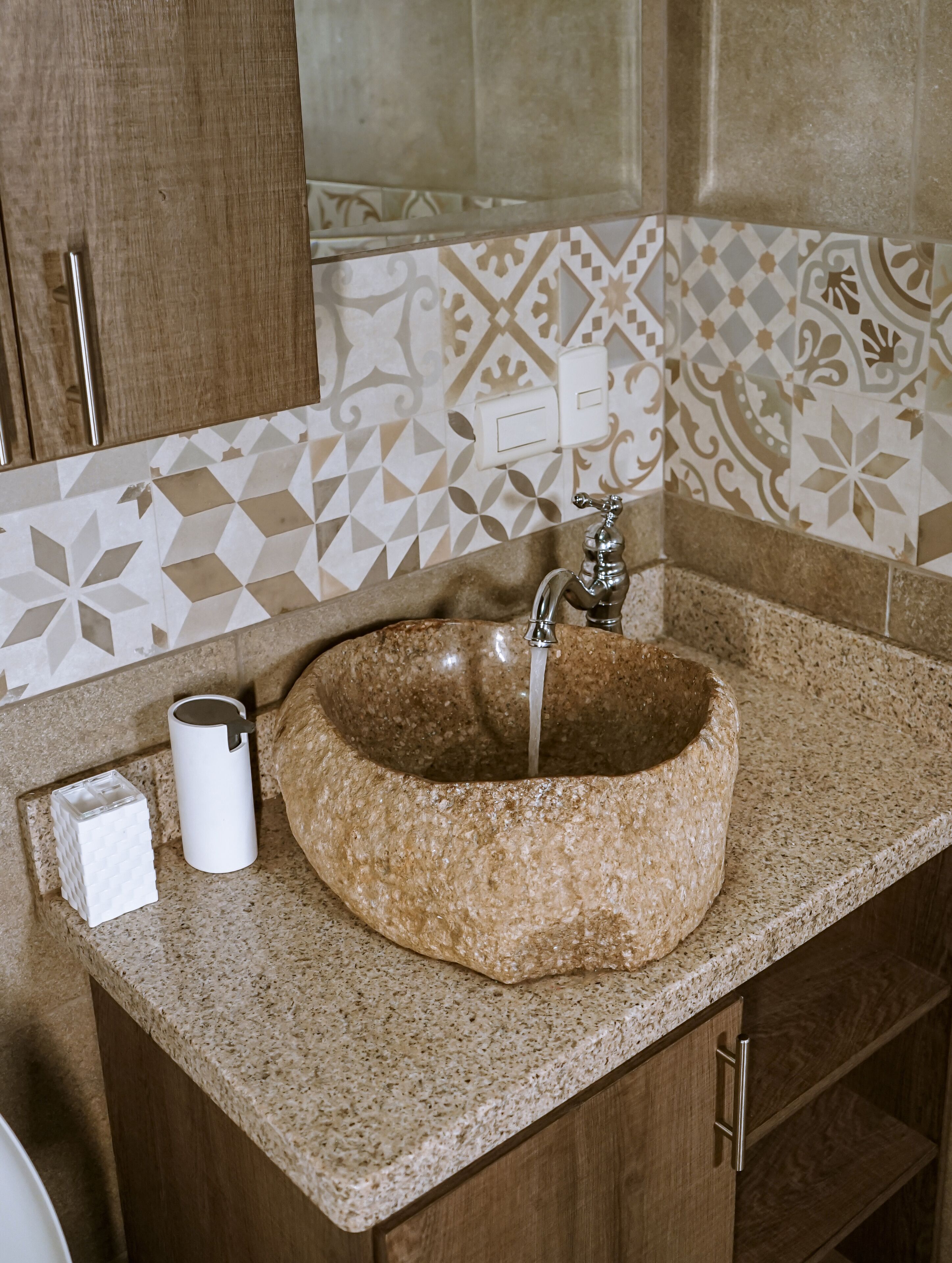 Un baño con lavamanos de granito, dispensador de toallas y azulejos estampados.