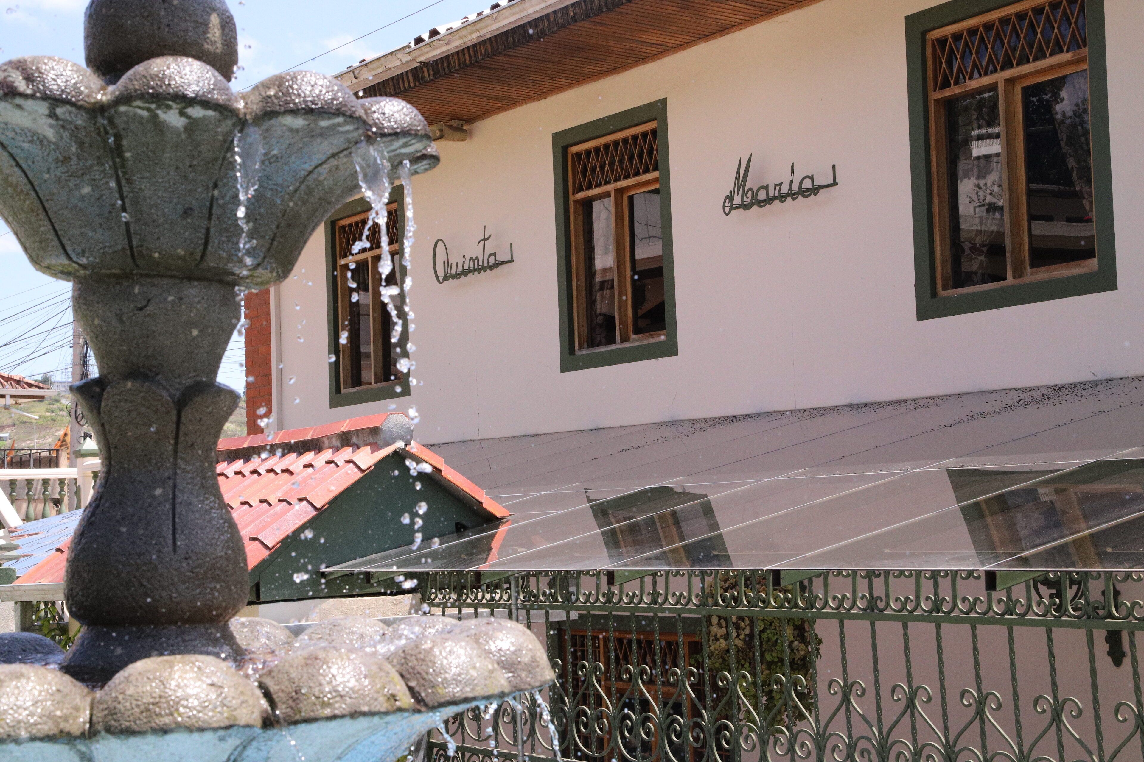 A building with a stone fountain in the foreground, a sign reading "Quinta," and a window with a lattice design.