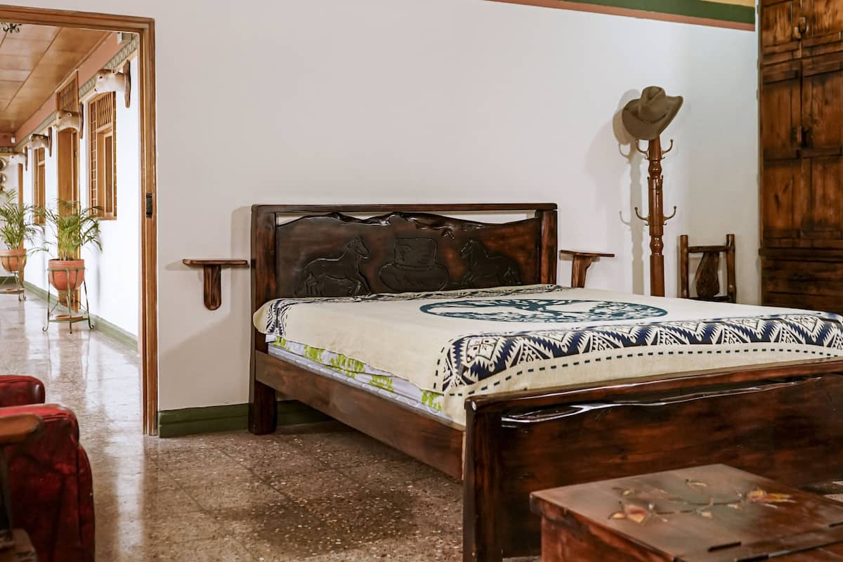 A traditional wooden bed with a patterned bedspread, a wooden nightstand, and a coat rack with a hat.
