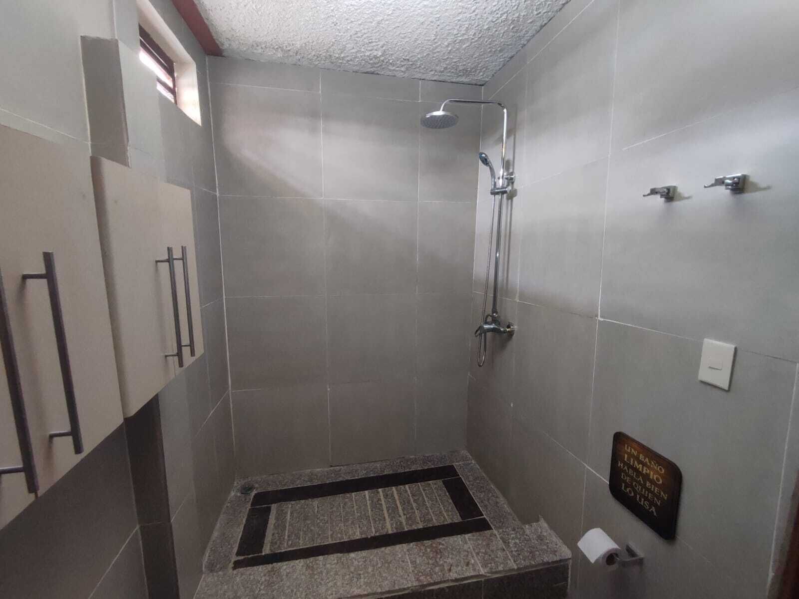 Uma casa de banho pequena revestida a azulejos, com um chuveiro, um apoio de mão e um ralo.